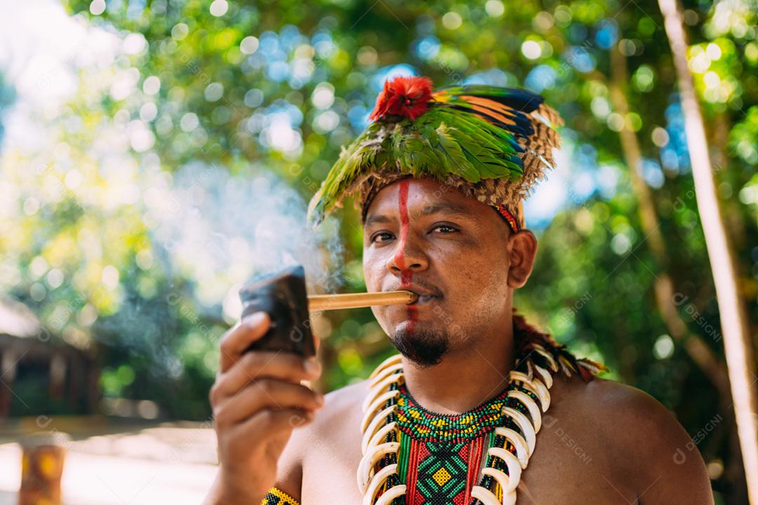 Chefe índio da tribo Pataxó fumando cachimbo. Índio brasileiro com cocar de penas e colar