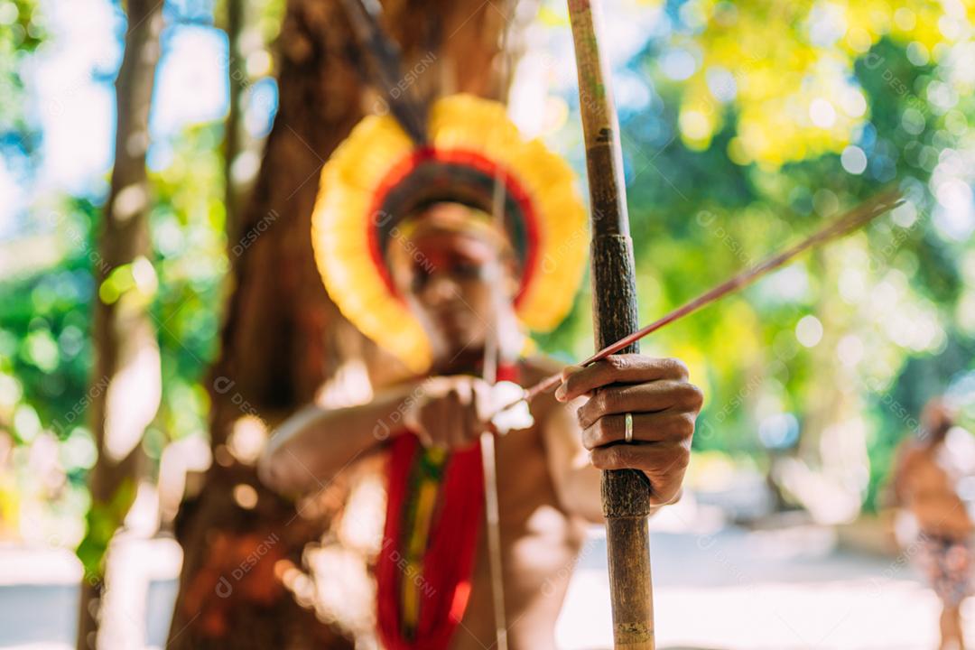 Índio da tribo Pataxó usando arco e flecha. Índio brasileiro com cocar de penas e colar