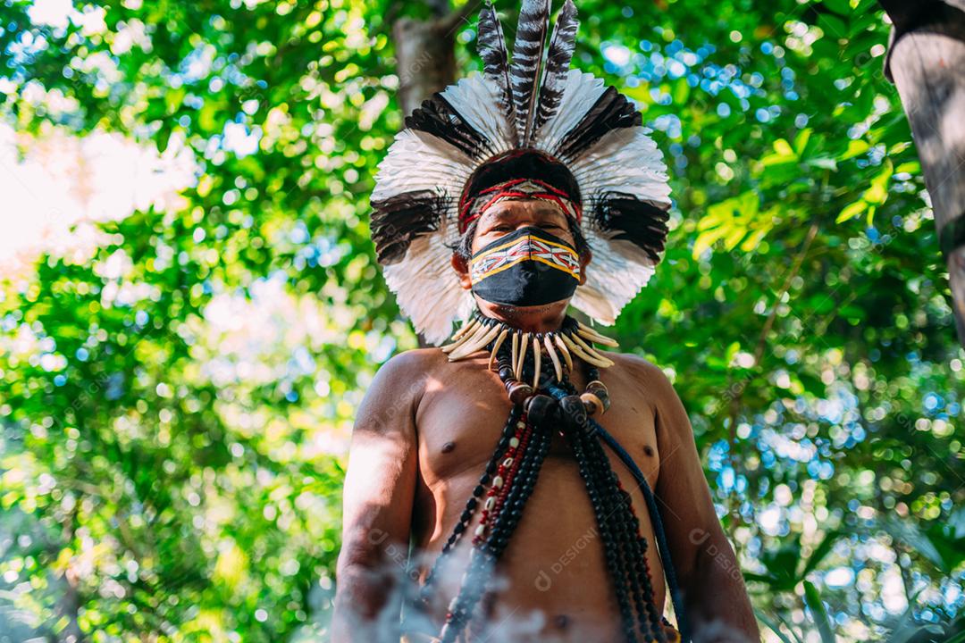 Xamã da tribo Pataxó. Homem indiano idoso usando cocar de penas e máscara facial devido à pandemia de covid-19