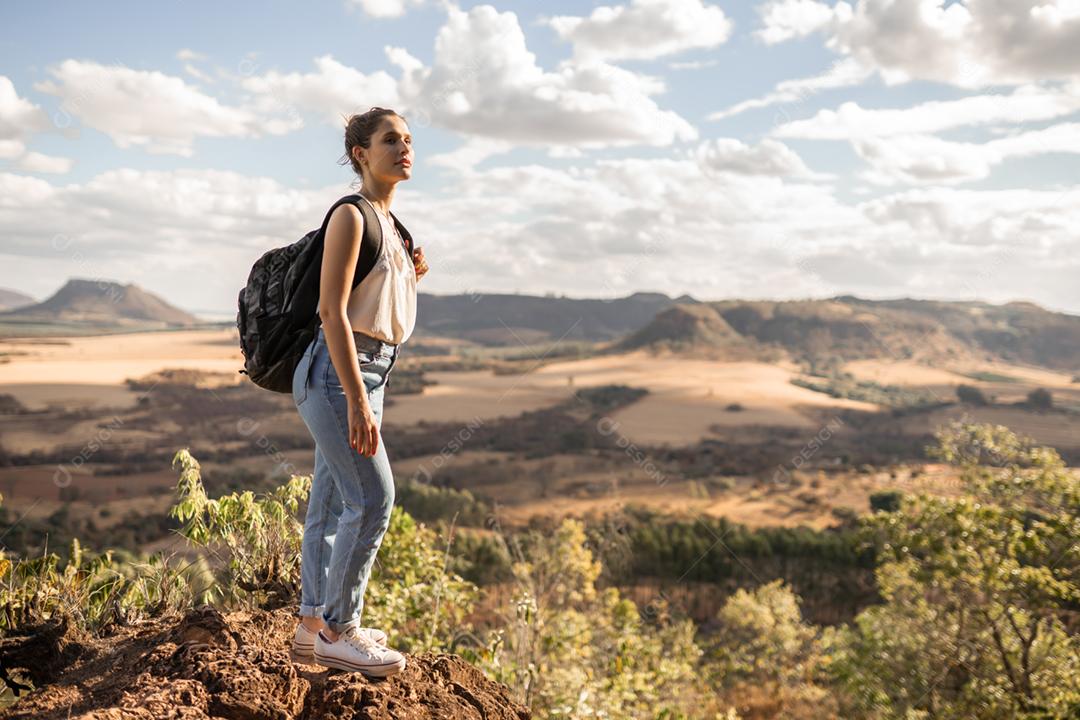 Jovem garota latina com mochila apreciando o pôr do sol no pico da montanha. Viajante de turista na paisagem do vale de fundo.