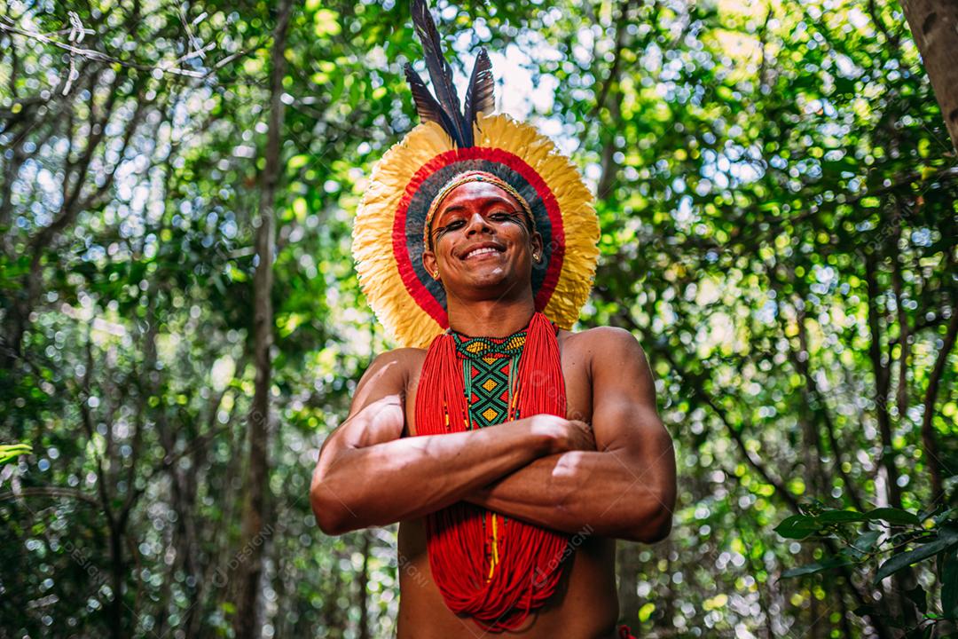 Índio da tribo Pataxó, com cocar de penas. Jovem índio brasileiro olhando para a câmera, sorrindo e braços cruzados