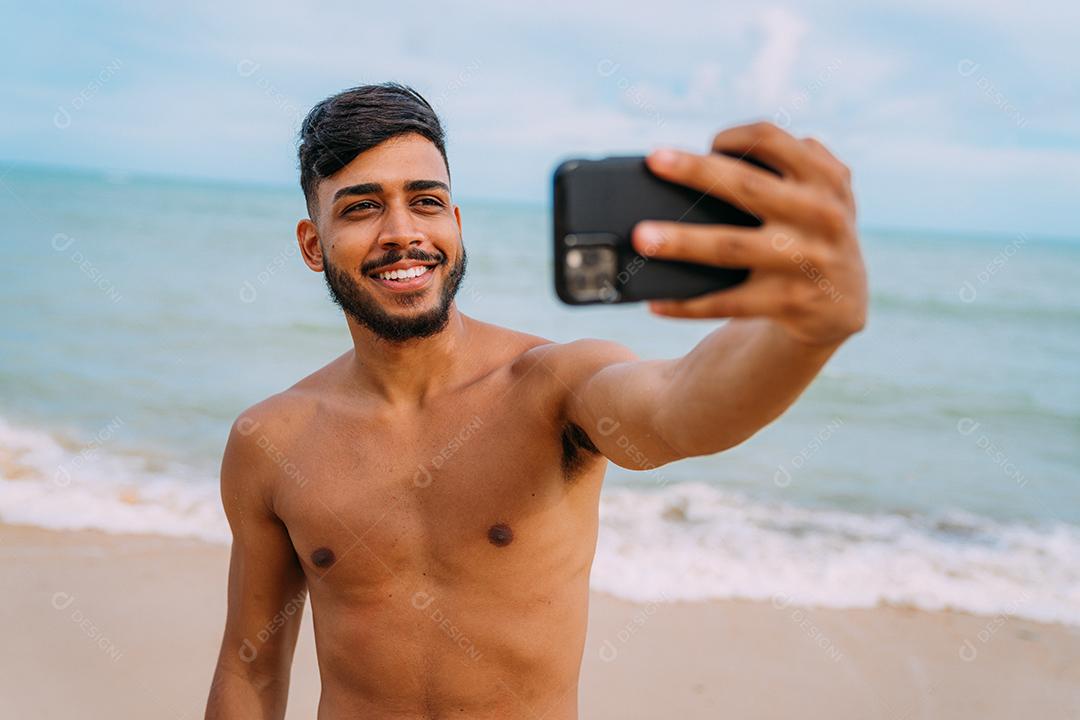 Feliz homem latino-americano fazendo selfie fundo de praia, ensolarado
