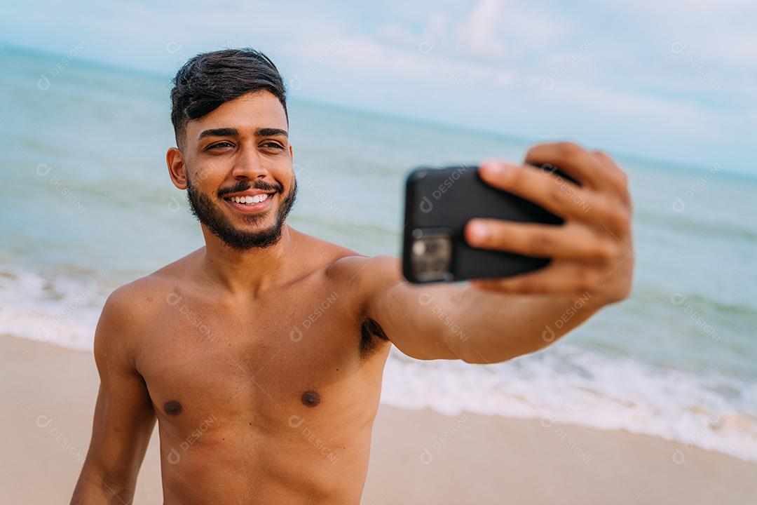 Feliz homem latino-americano fazendo selfie fundo de praia, ensolarado