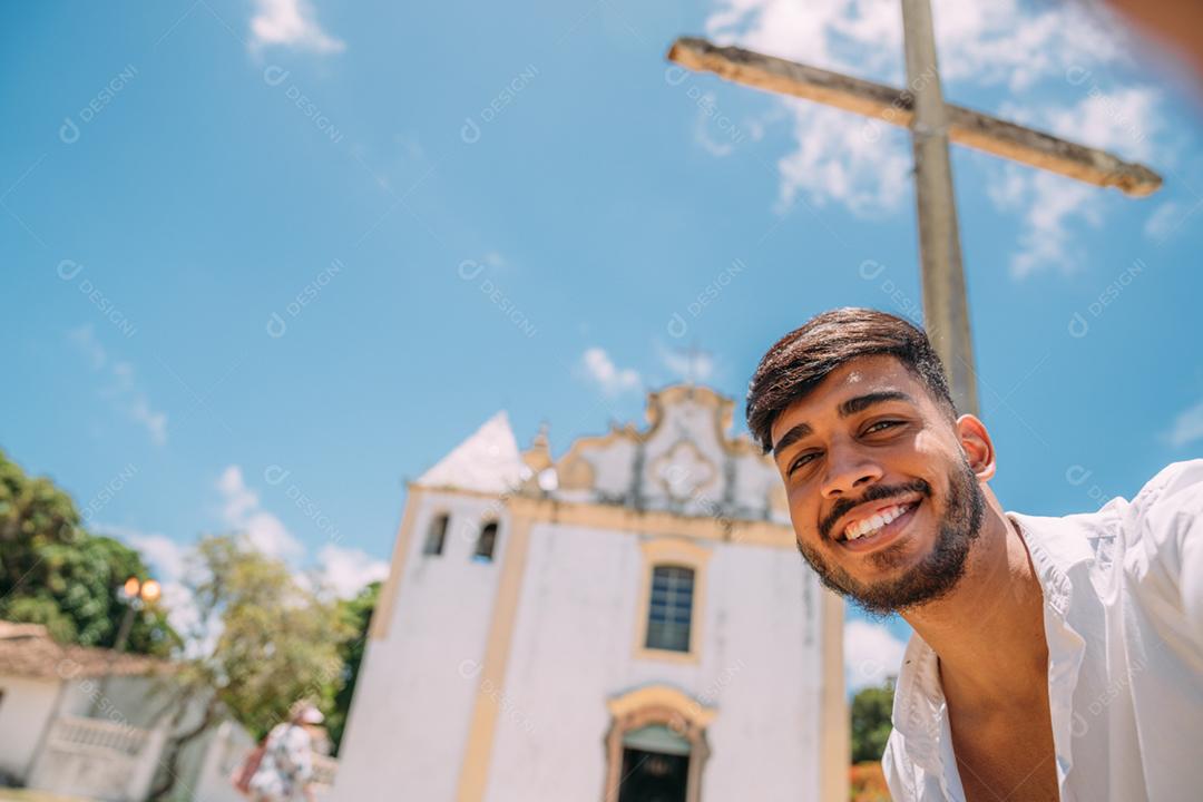 Amigável jovem latino-americano sorrindo para a câmera. Turista tirando uma selfie com a igreja de Nossa Senhora