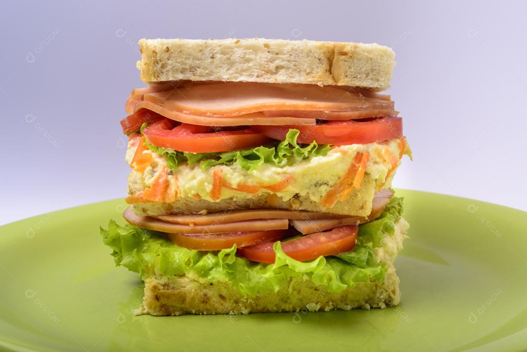 Sanduíche grande com presunto defumado, com alface e tomate na chapa verde. Comida rápida.