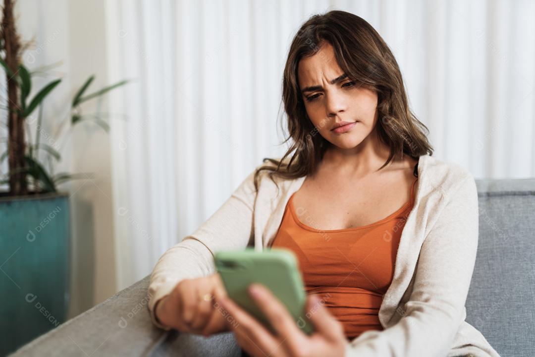 Feliz dama latina relaxa em casa sozinha, sente-se na sala e compartilhe boas notícias nas mídias sociais via celular