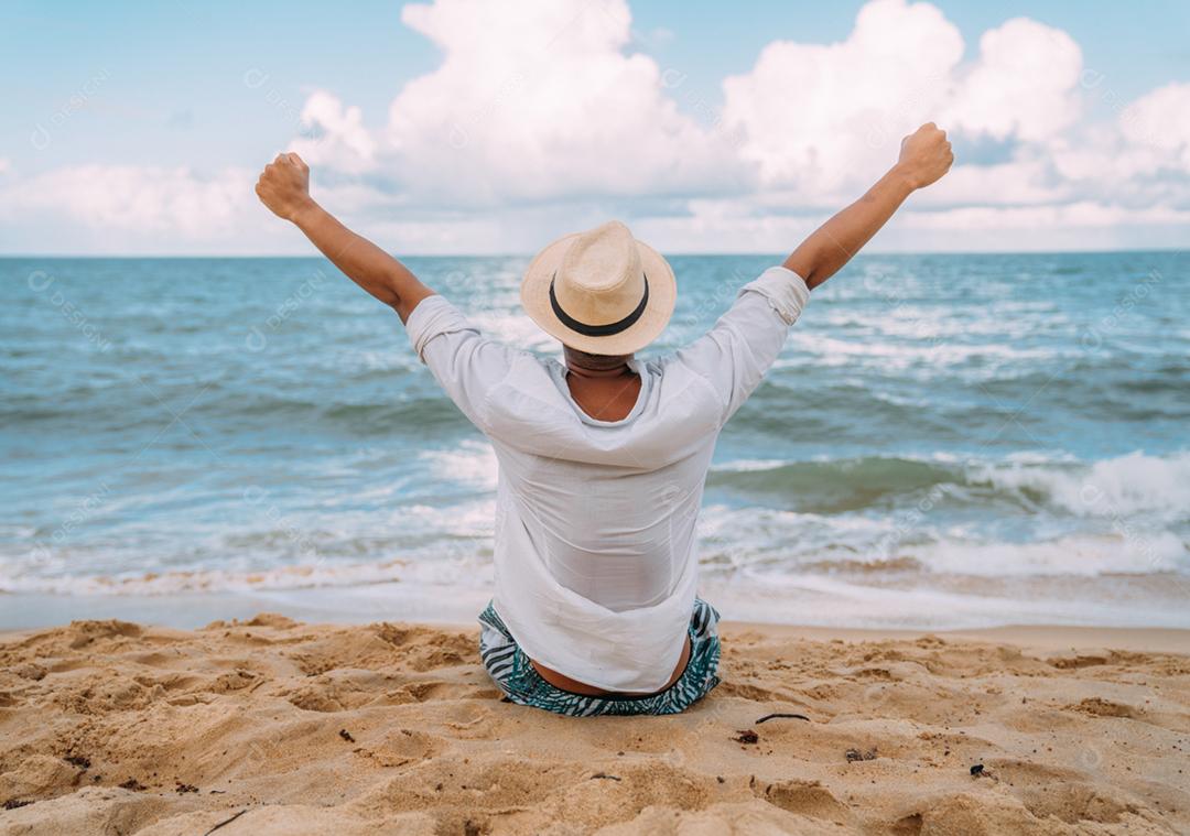 Silhueta de um jovem na praia. homem latino-americano sentado na areia da praia, usando um chapéu o