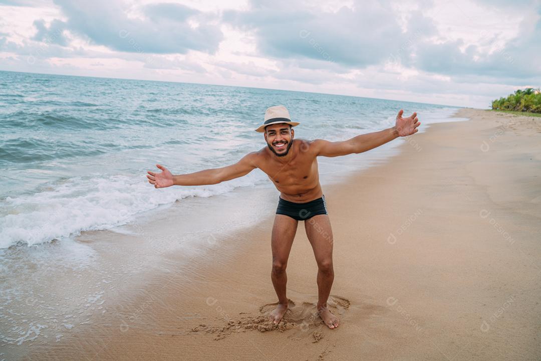 Amigável confiante e sorridente jovem latino-americano olhando para a câmera na praia