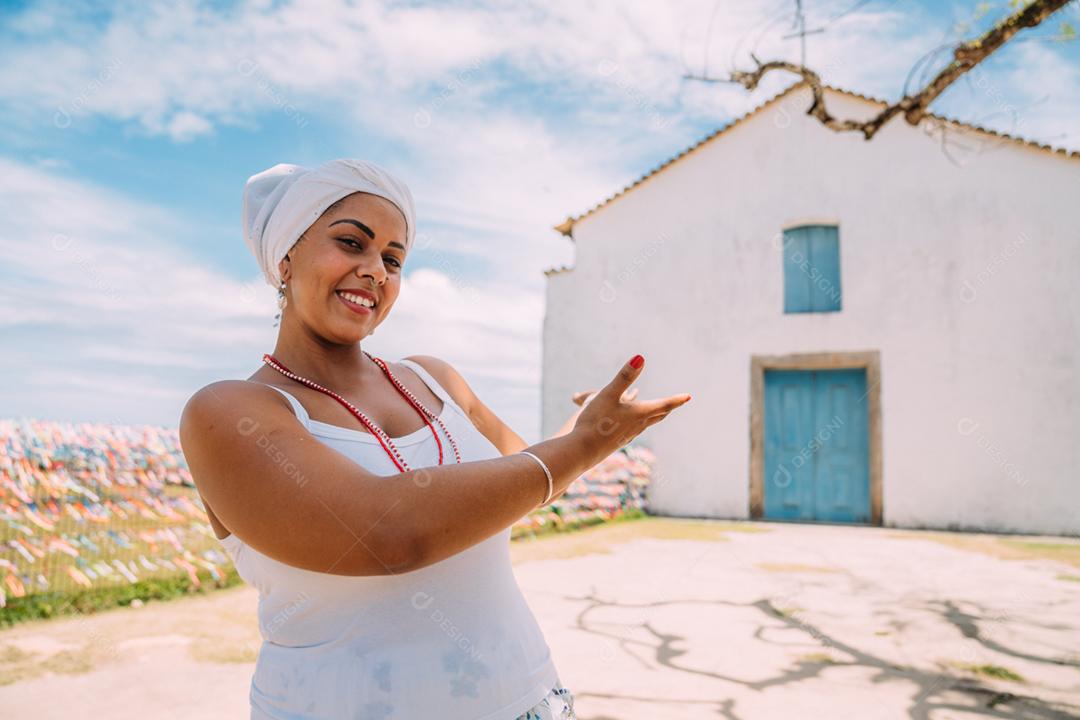 Feliz mulher brasileira vestida com traje tradicional baiano, braços cruzados no centro histórico de Porto Seguro ao fundo