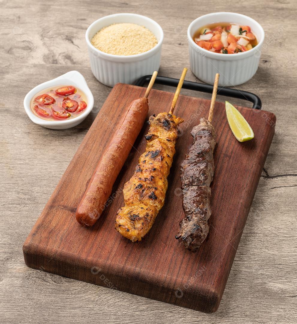 Espetos de carne, frango e salsicha de porco sobre tábua de madeira