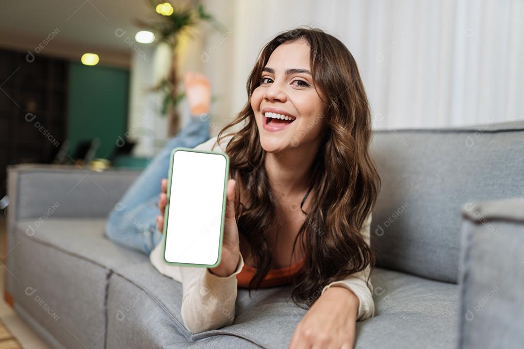 Feliz dama latina relaxa em casa sozinha, sente-se na sala e compartilhe boas notícias nas mídias sociais via celular