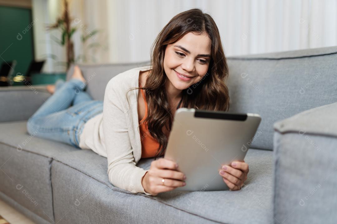 A senhora latina feliz relaxa em casa sozinha na pose do quarto compartilha boas notícias nas mídias sociais via tablet digital