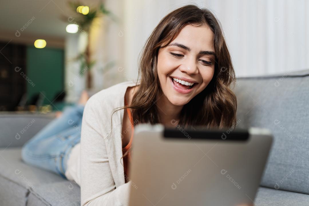 A senhora latina feliz relaxa em casa sozinha na pose do quarto compartilha boas notícias nas mídias sociais via tablet digital