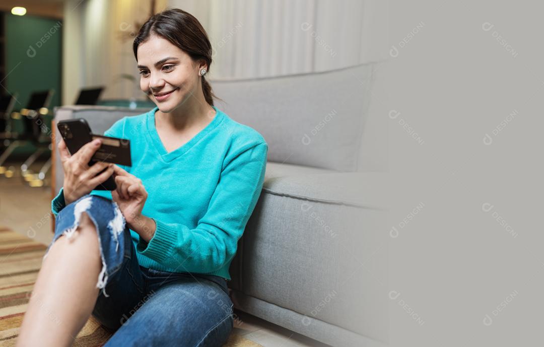 O cliente sorridente da senhora latina segura o cartão de crédito do telefone móvel para fazer compras on-line