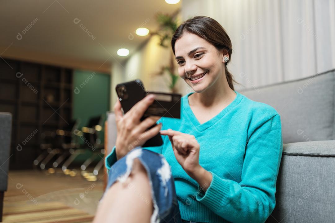 O cliente sorridente da senhora latina segura o cartão de crédito do telefone móvel para fazer compras on-line