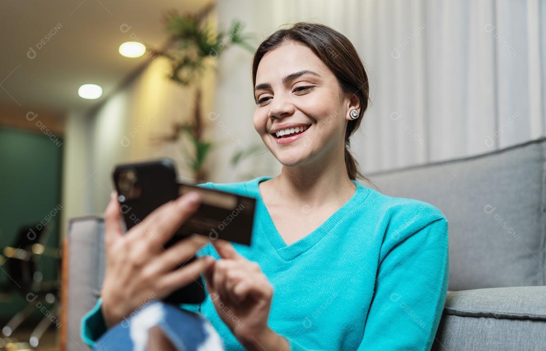 O cliente sorridente da senhora latina segura o cartão de crédito do telefone móvel para fazer compras on-line