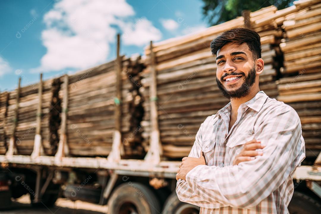 Retrato de jovem latino trabalhando ao lado de troncos de árvores no caminhão.