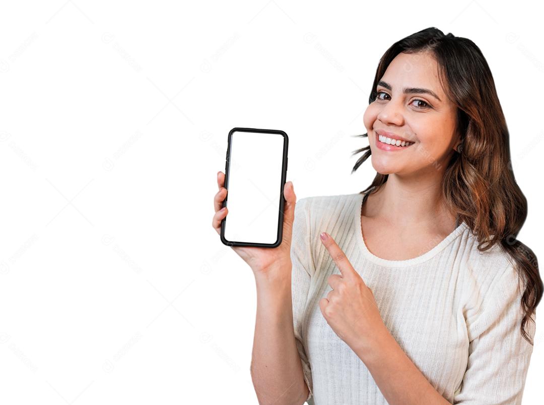 Muito jovem Latina apontando smartphone em pé no fundo branco isolado se sentindo feliz.