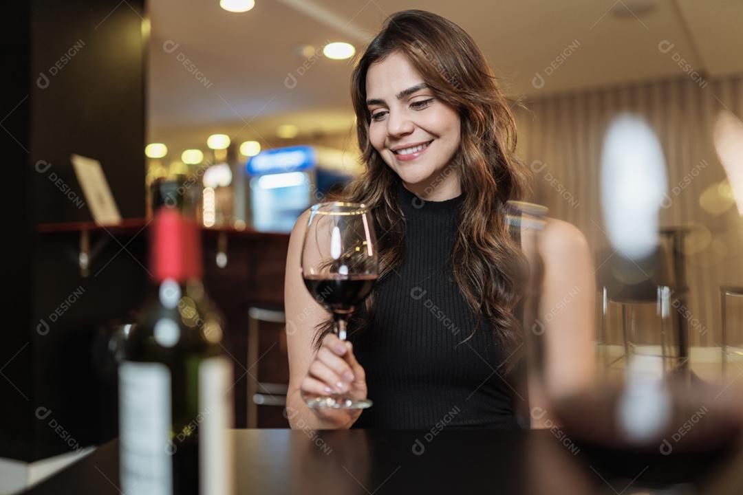 Jovem mulher latina com um copo de vinho tinto no bar