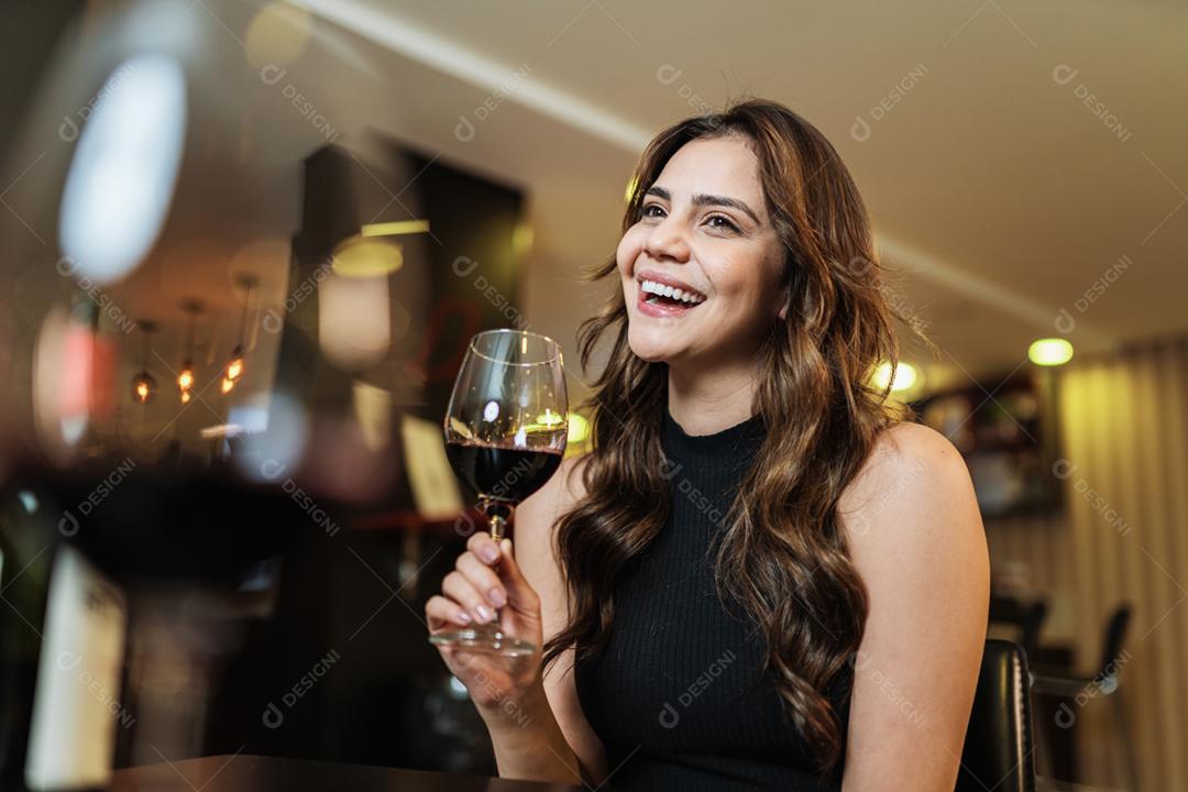 Jovem mulher latina com um copo de vinho tinto no bar