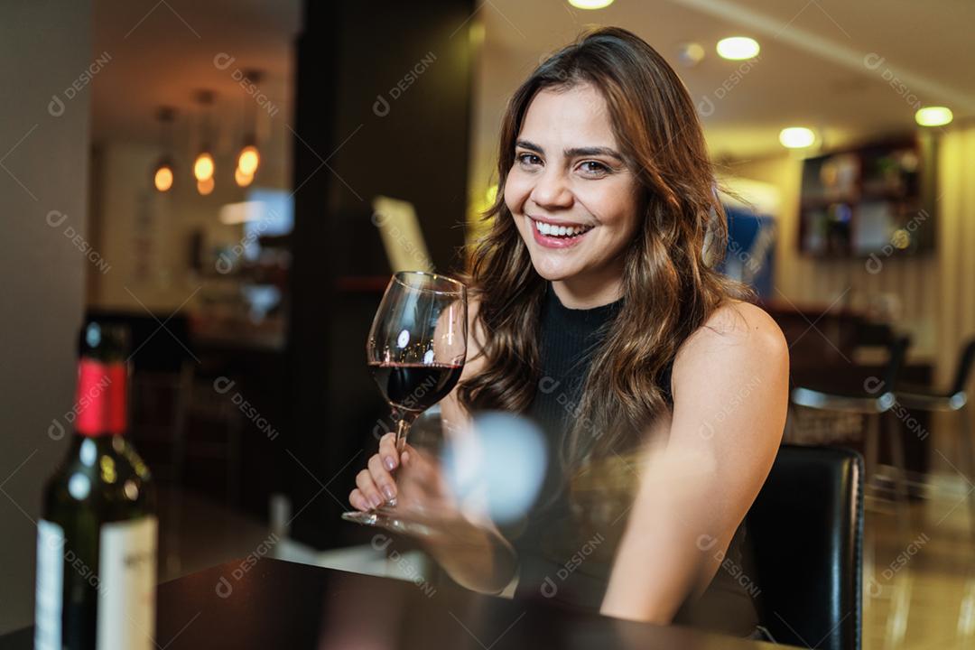 Jovem mulher latina com um copo de vinho tinto no bar