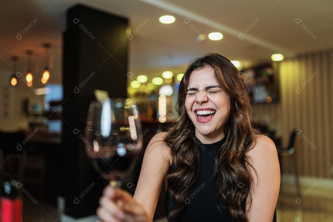 Jovem mulher latina com um copo de vinho tinto no bar