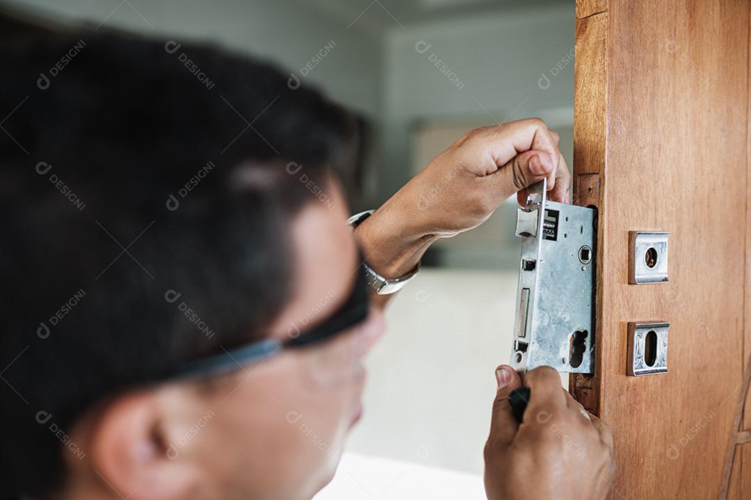 Close-up de mãos masculinas reparando ou instalando uma fechadura de porta de metal.