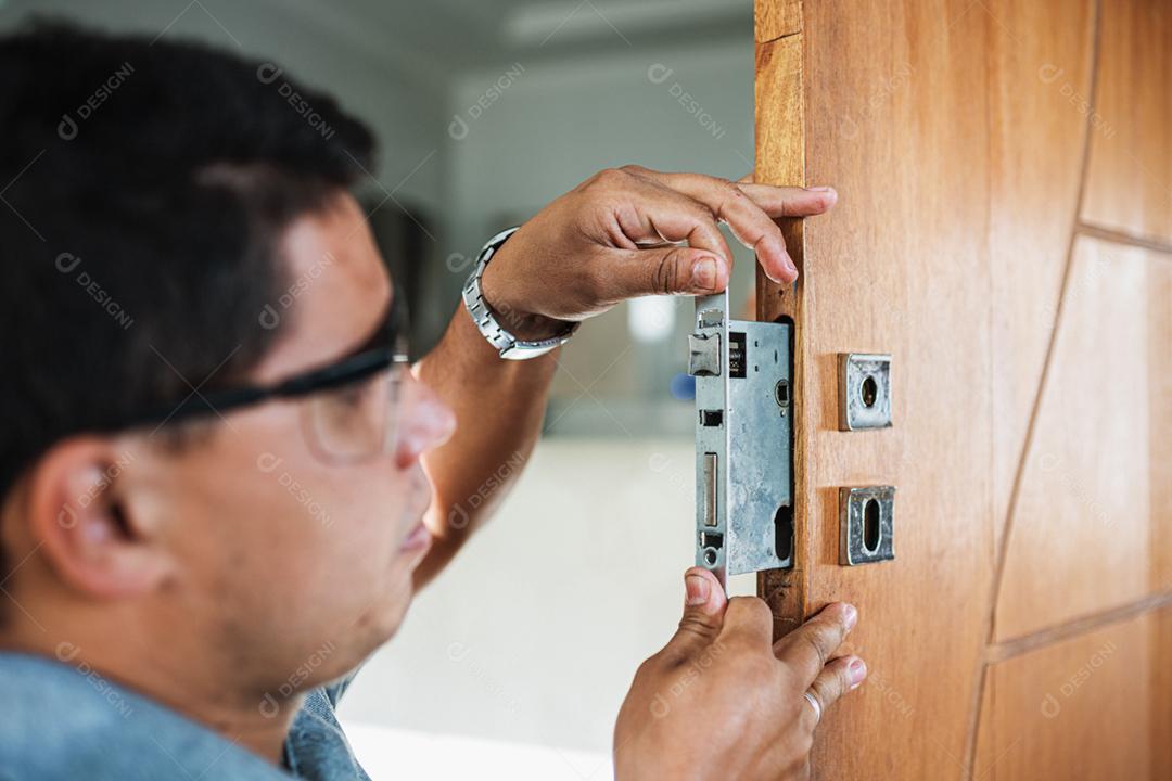 Close-up de mãos masculinas reparando ou instalando uma fechadura de porta de metal.