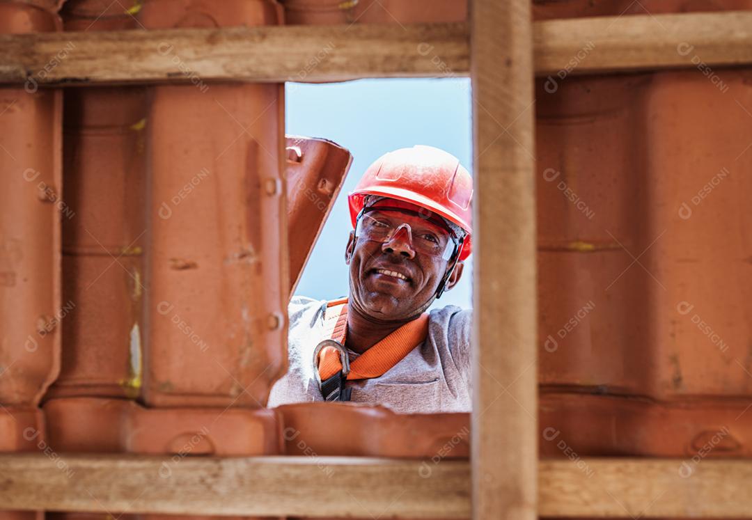 Trabalhador latino instalando telhas cerâmicas amarelas montadas em placas de madeira cobrindo telhado