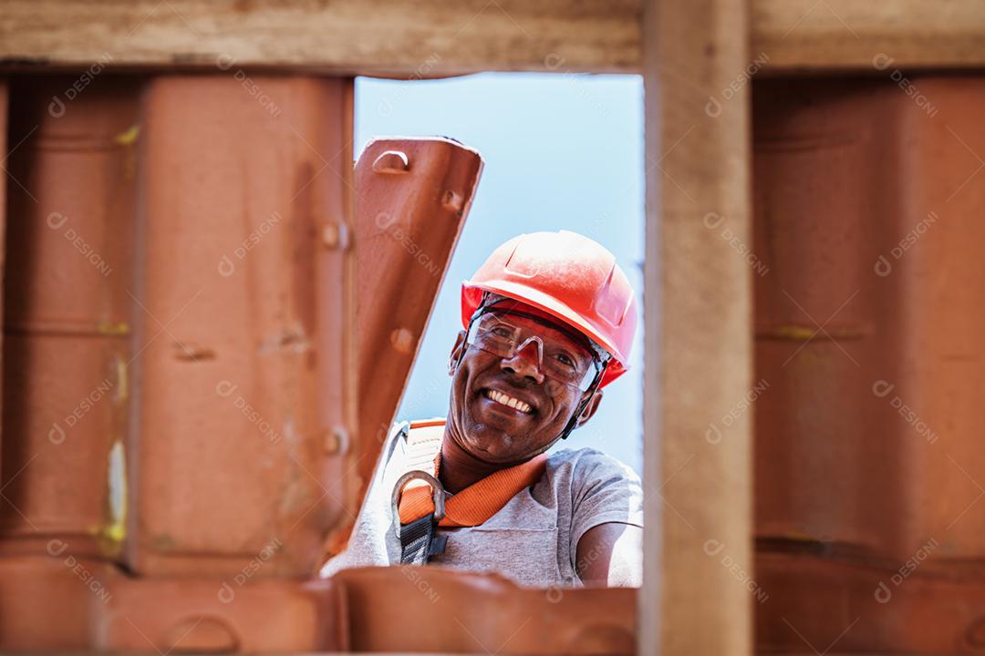 Trabalhador latino instalando telhas cerâmicas amarelas montadas em placas de madeira cobrindo telhado