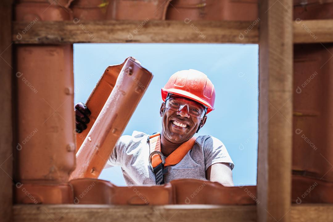 Trabalhador latino instalando telhas cerâmicas amarelas montadas em placas de madeira cobrindo telhado