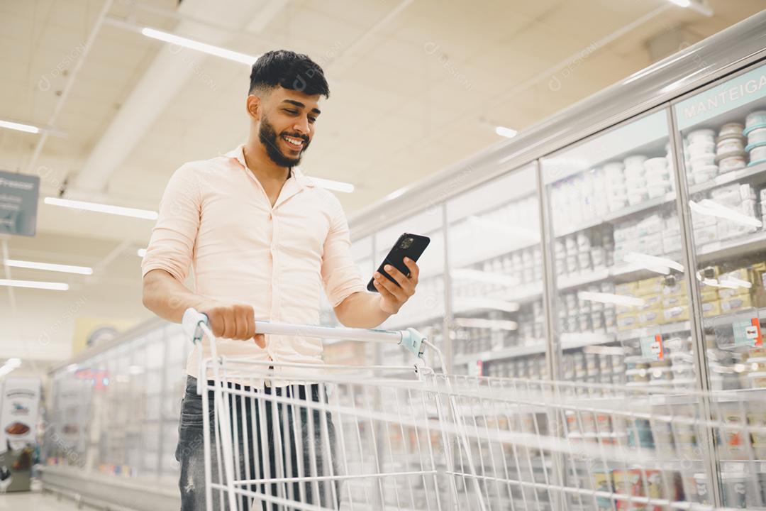 Bonito homem latino-americano usa smartphone no supermercado