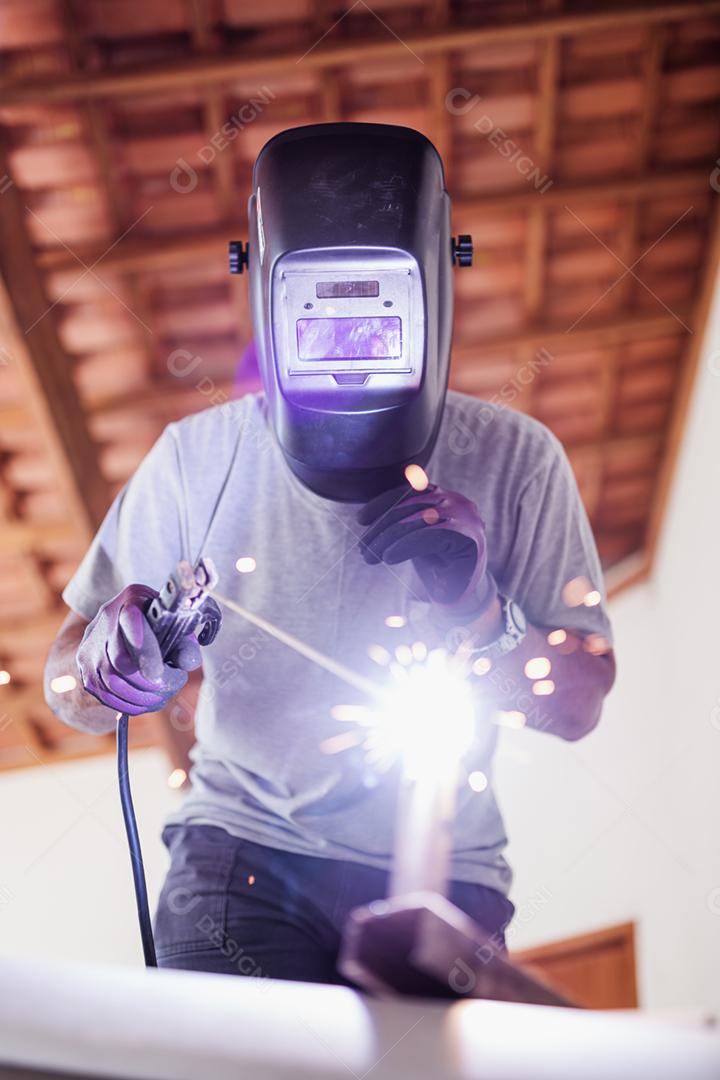 Feche a vista do retrato do soldador de máscara profissional protegido trabalhando em escultura de metal em uma casa em construção.