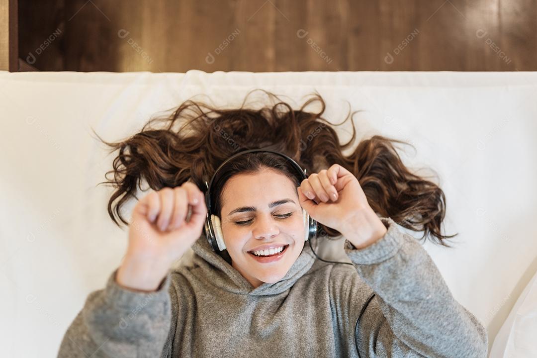 Mulher latina feliz usar fones de ouvido deitado na cama ouvindo música
