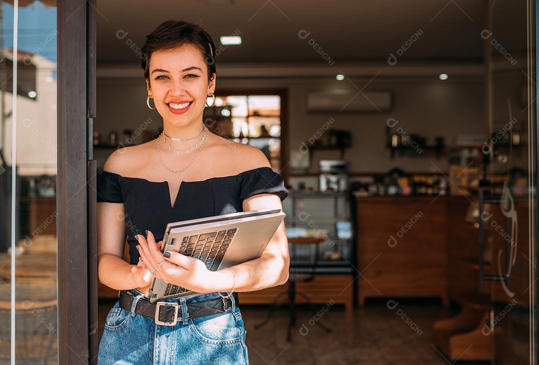 Retrato de uma mulher latina feliz parada na porta de sua loja.