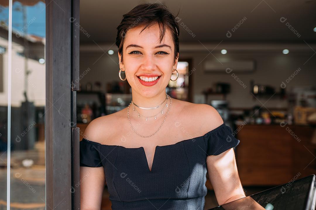 Retrato de uma mulher latina feliz parada na porta de sua loja.