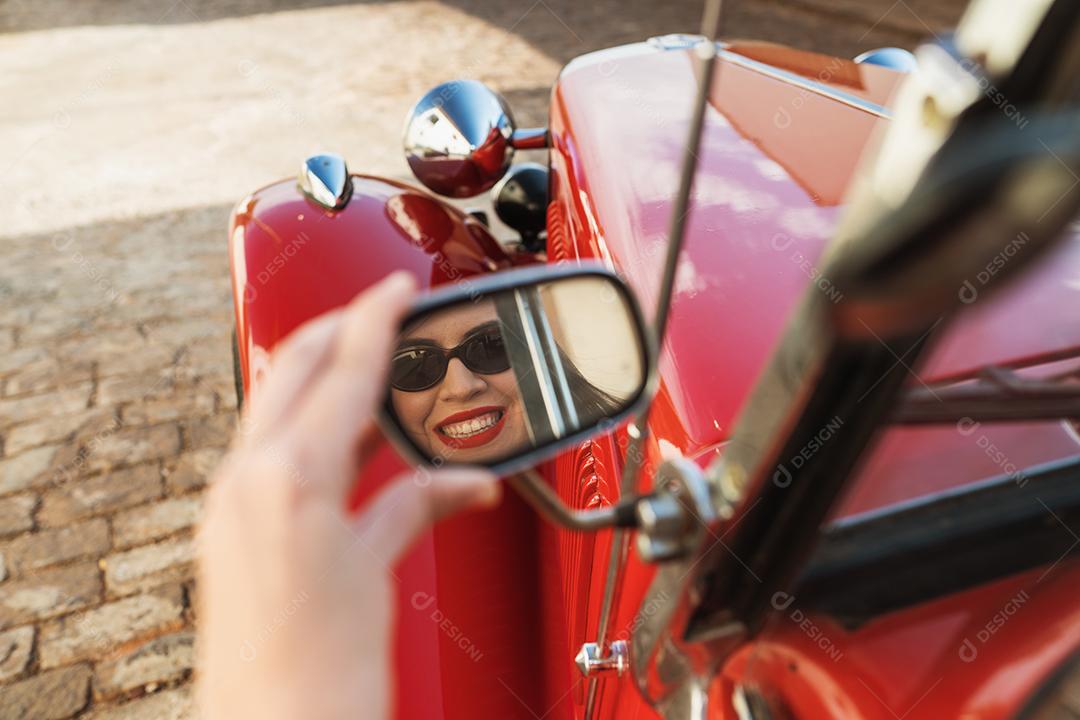 Reflexo da garota sentada dentro do velho carro vermelho, motorista feliz.
