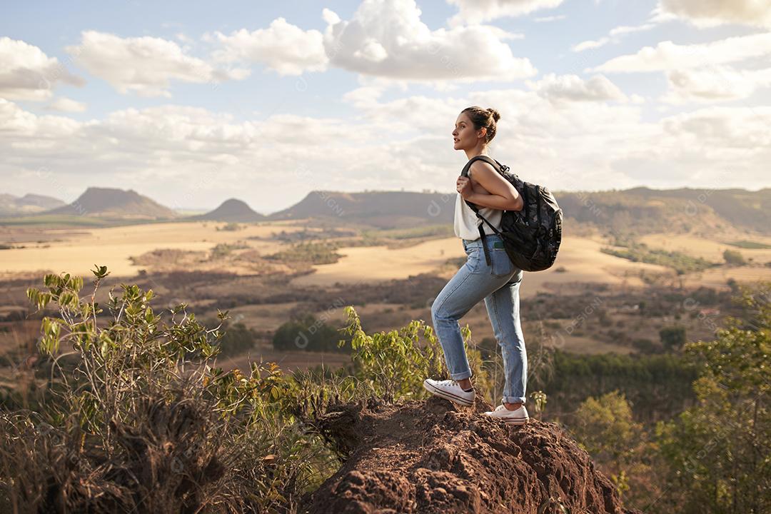 Jovem latina com mochila curtindo o pôr do sol no pico de montanha