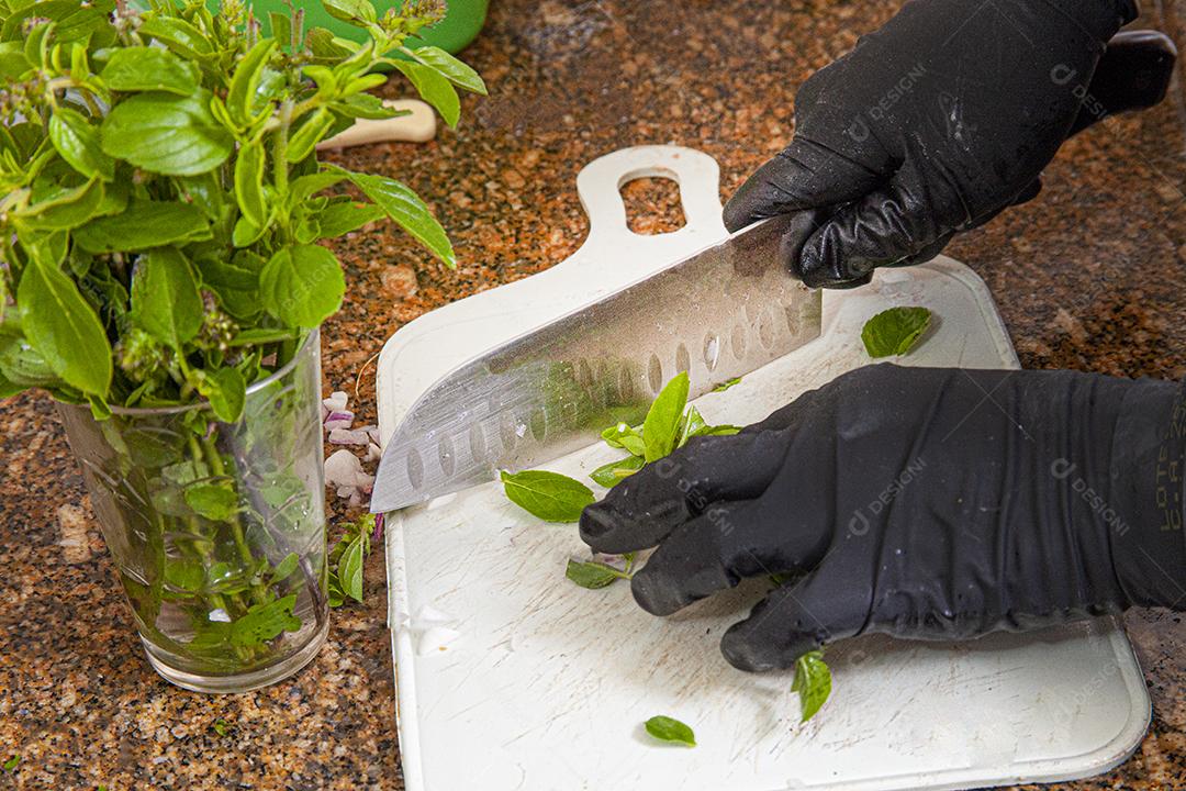 Pessoas usando luvas pretas cortando folhas em uma tabua