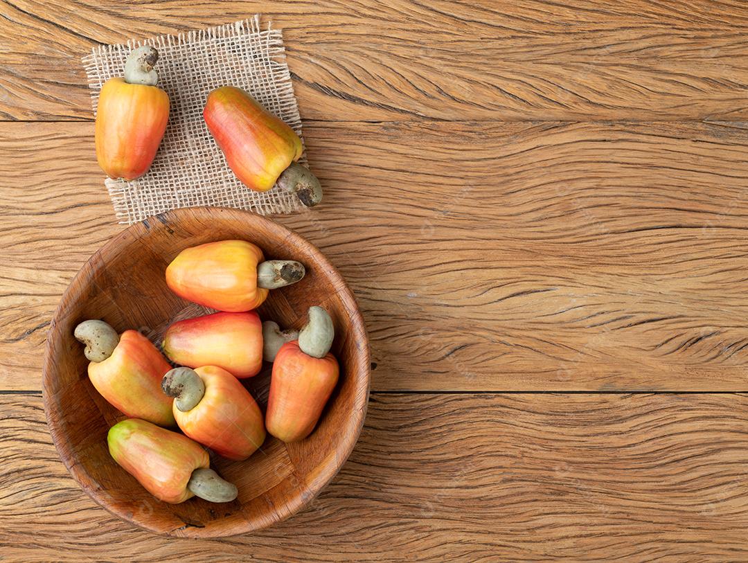 Um grupo de frutas de caju em uma tigela sobre mesa de madeira