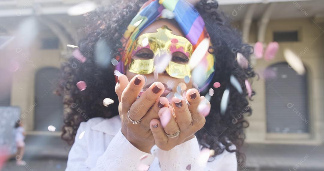 Festa carnavalesca. Mulher brasileira de cabelo encaracolado fantasiada soprando confetes.