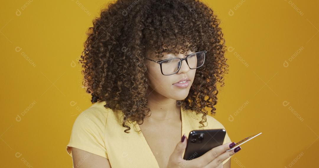 Mulher jovem e bonita segurando smartphone e cartão de banco de crédito. Transação de compras on-line.