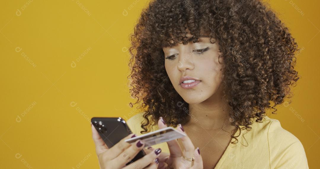 Mulher jovem e bonita segurando smartphone e cartão de banco de crédito. Transação de compras on-line