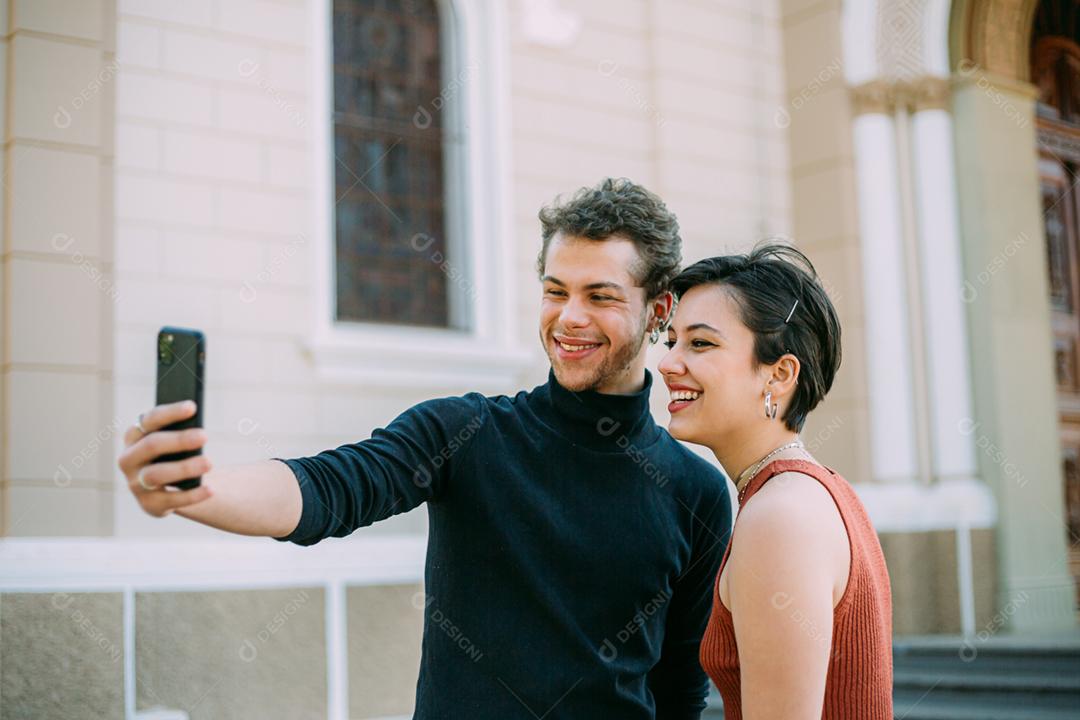 Casal latino andando na cidade usando smartphone ao ar livre.