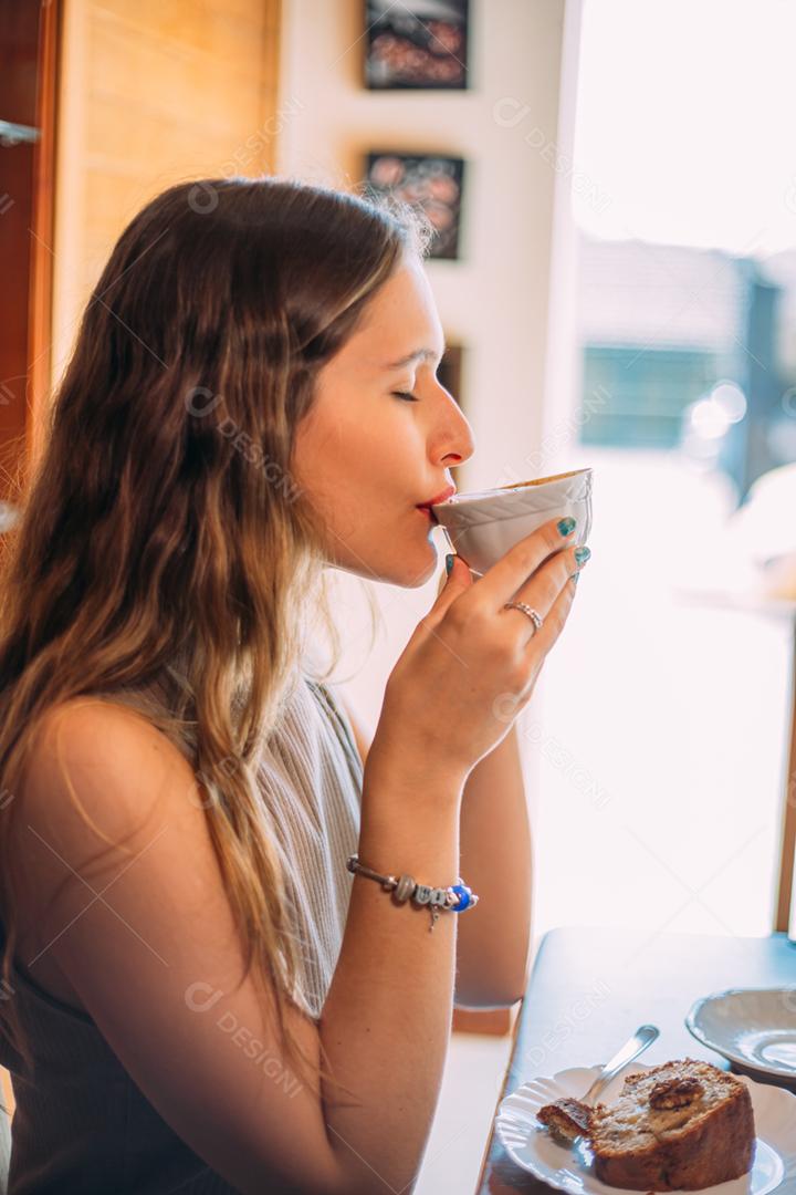 Jovem e linda mulher latina feliz com cabelos longos e encaracolados desfrutando de cappuccino em um café de rua