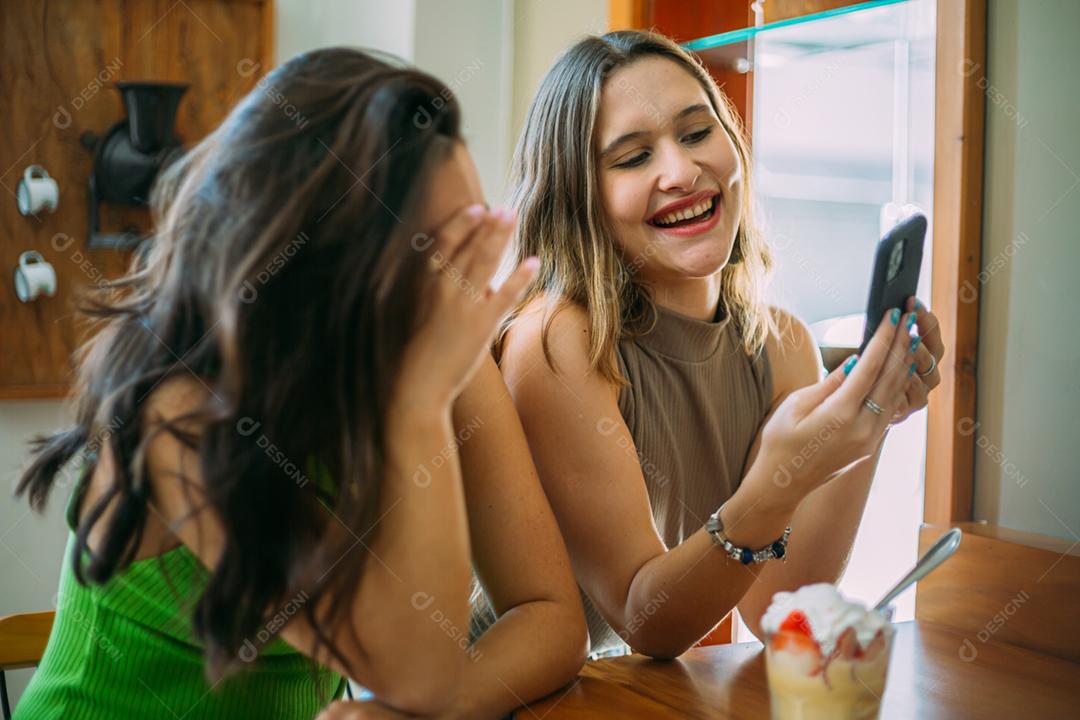 Animadas lindas duas mulheres latinas assistem a um vídeo engraçado no celular moderno, têm expressões