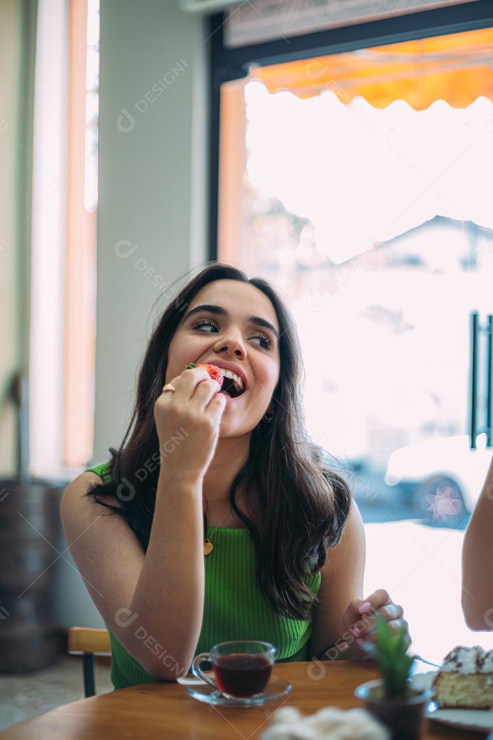 Linda jovem latina comendo um morango em uma loja de café.