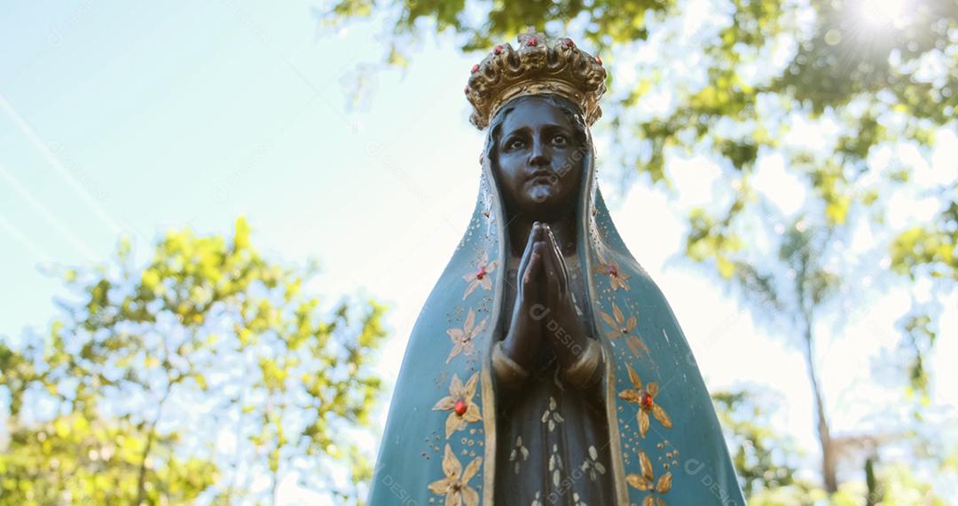 Escultura da imagem de Nossa Senhora Aparecida padroeira do Brasil. Imagem com gimbal no fundo da natureza em dia ensolarado.