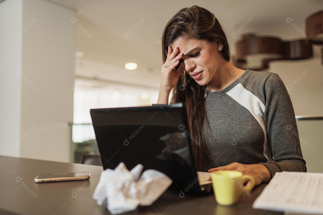 Mulher latina estressada que sofre de enxaqueca com um laptop sentado em uma mesa em casa