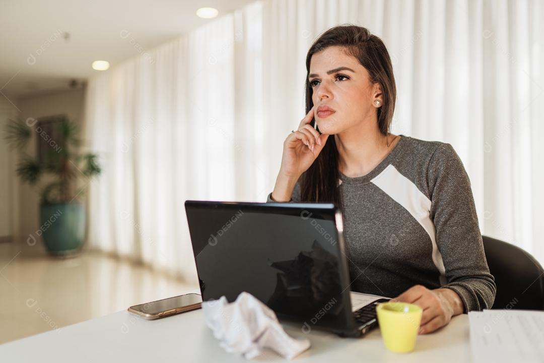 Jovem linda brasileira trabalhando com laptop enquanto está sentado na mesa de escritório, trabalhando em casa conceito.